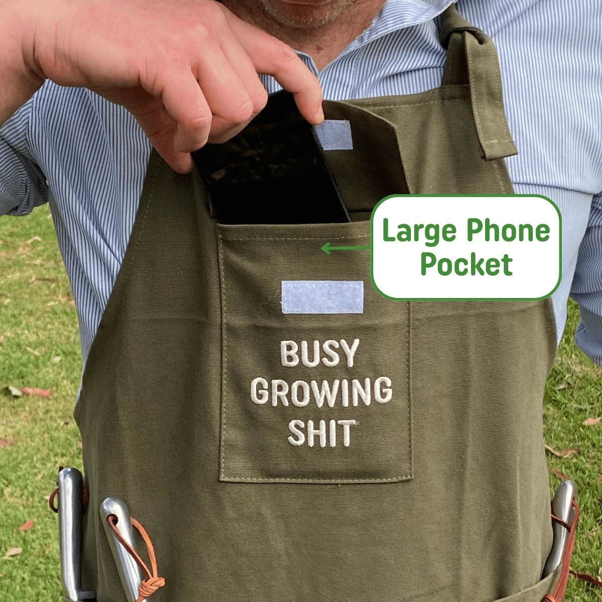 Person wearing a green apron with a large phone pocket and text, standing outdoors.