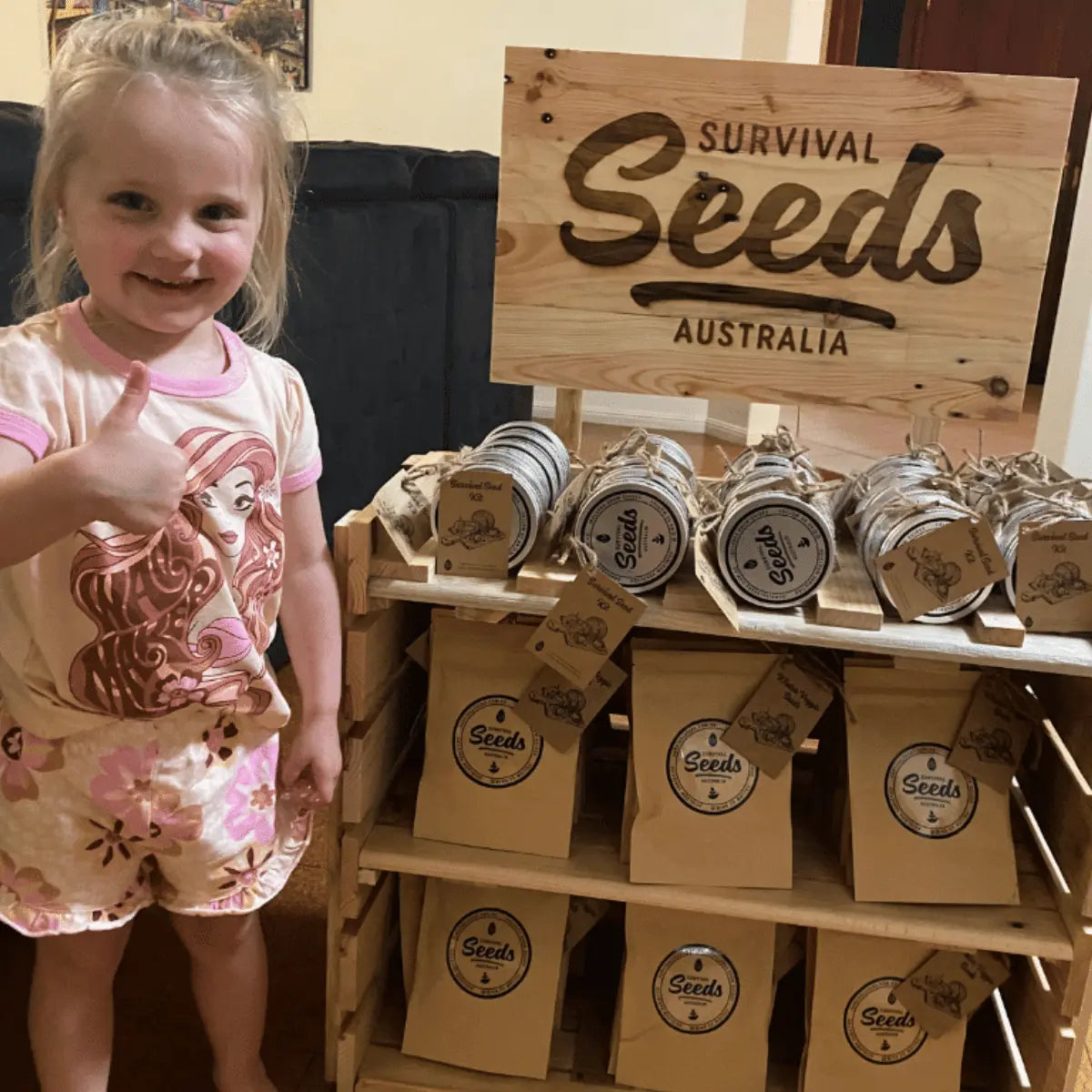 little girl thumbs up standing beside Survival Seeds mini stall