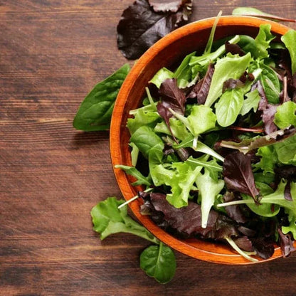 Leafy greens seeds variety in a wooden bowl, showcasing fresh salad greens on a rustic wooden table.