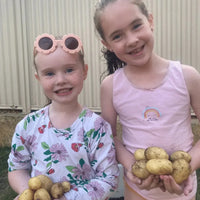 Two smiling children holding freshly harvested potatoes from Seeds for Kids gardening kits.