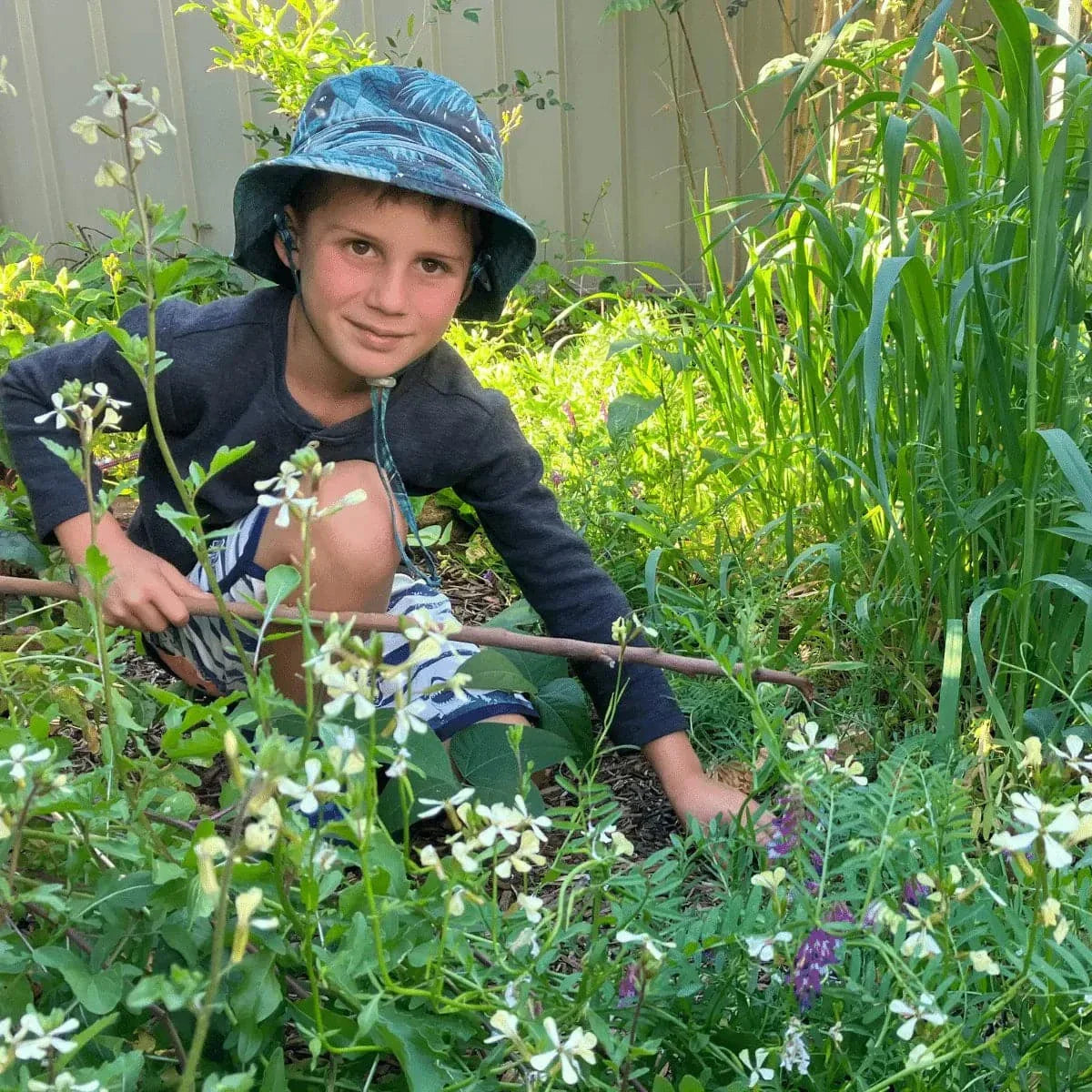 Child enjoying gardening with "Seeds for Kids" kit, surrounded by plants.