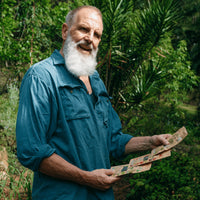 Elderly man in garden holding packets of leafy greens seeds.